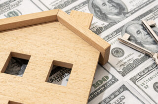 Wooden house and keys on top of money