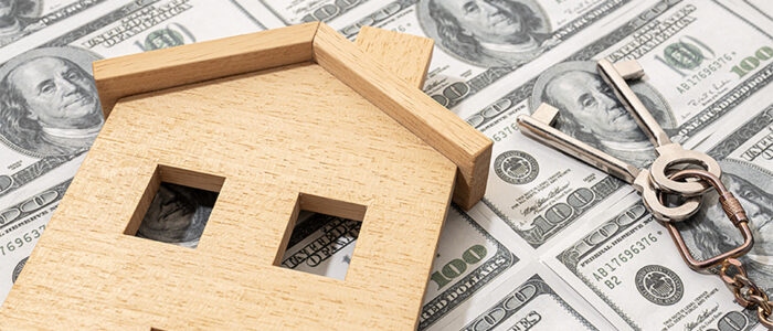 Wooden house and keys on top of money