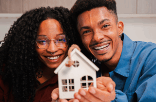 Young African American couple smiling and looking at camera, holding a toy house and the keys