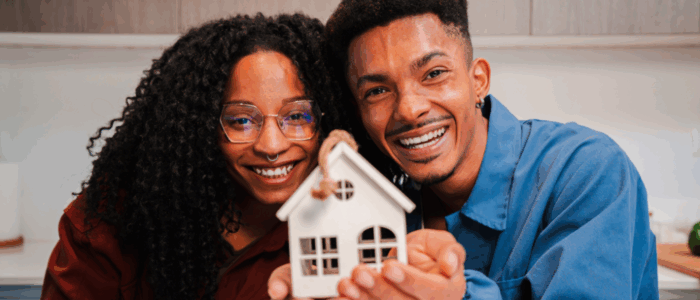 Young African American couple smiling and looking at camera, holding a toy house and the keys