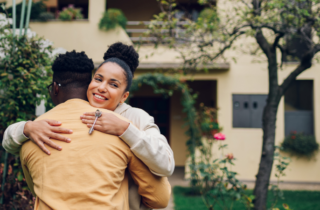 Woman Hugs Partner in Front of House